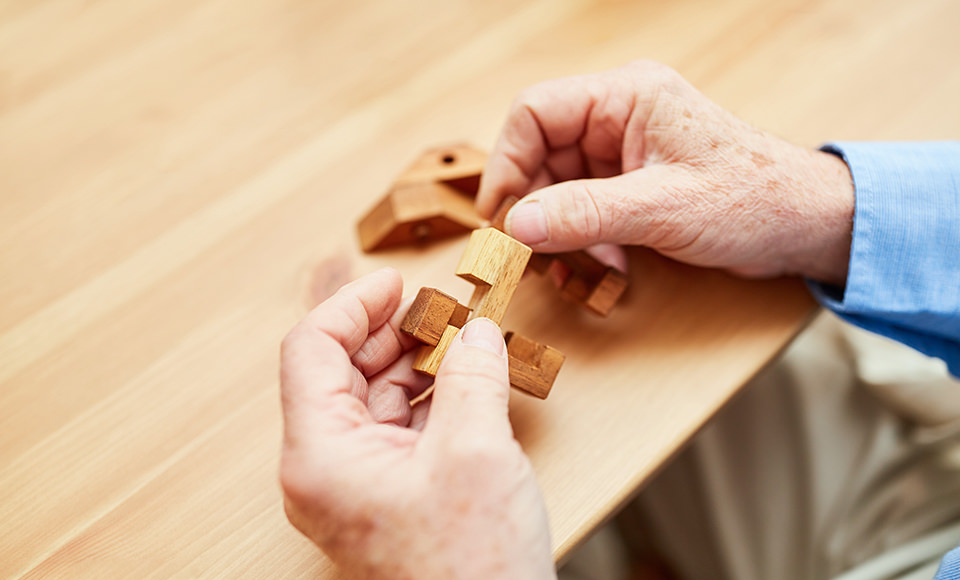 Hands of an old man put wooden building blocks together as a patience game
